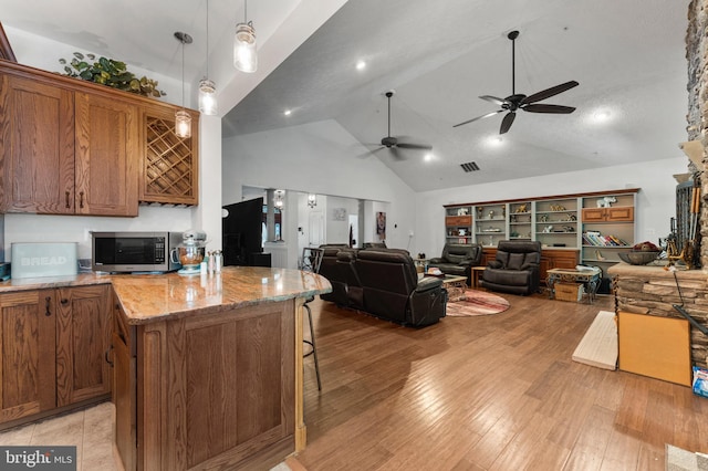 6707 Burch Hill Rd, Brandywine, MD 20613 - kitchen with stainless steel microwave, brown cabinetry, high vaulted ceiling, a ceiling fan, and open floor plan