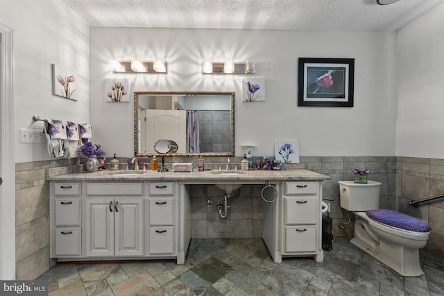 6707 Burch Hill Rd, Brandywine, MD 20613 - bathroom with tile walls, a textured ceiling, toilet, double vanity, and wainscoting