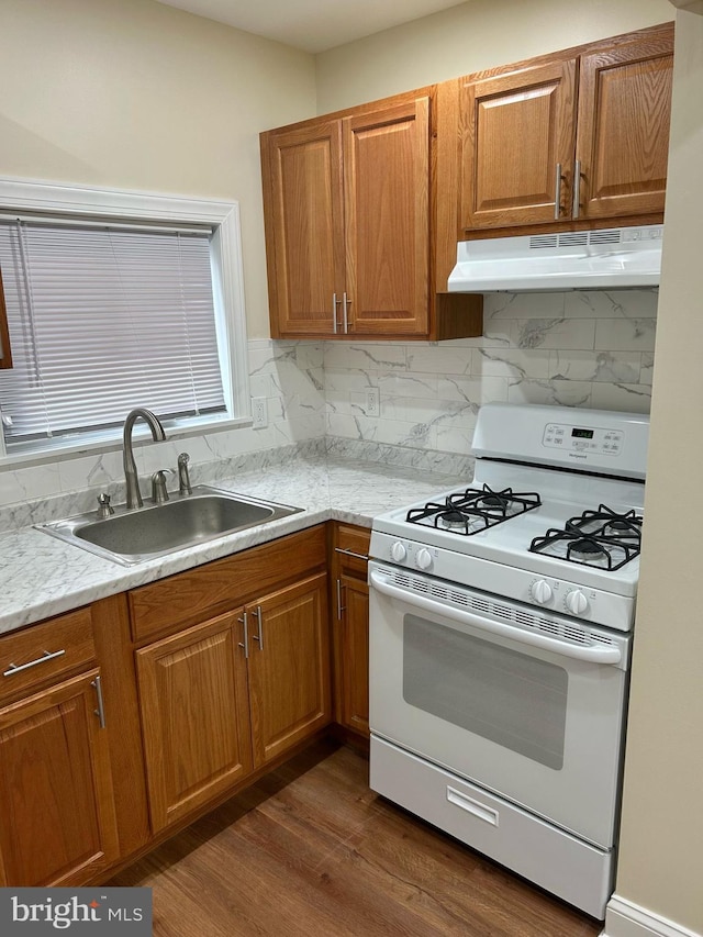 kitchen with brown cabinets, decorative backsplash, a sink, white range with gas cooktop, and under cabinet range hood