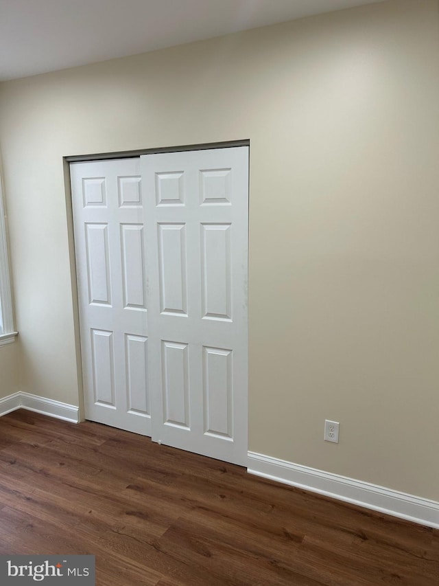 unfurnished bedroom with dark wood-style floors, baseboards, and a closet