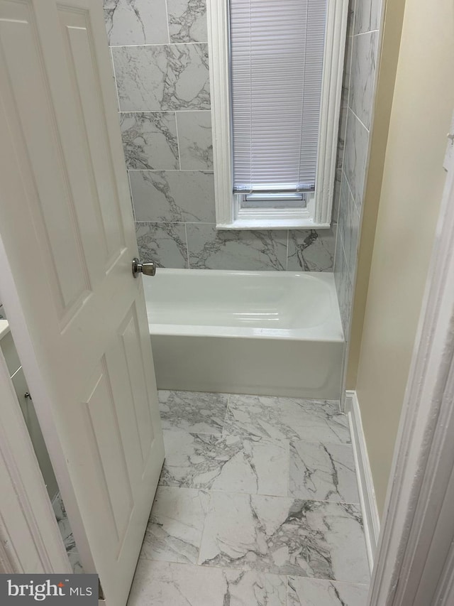bathroom with baseboards, a tub, and marble finish floor