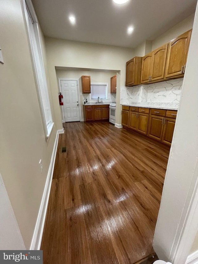 kitchen featuring decorative backsplash, brown cabinetry, white gas range oven, dark wood-style flooring, and visible vents