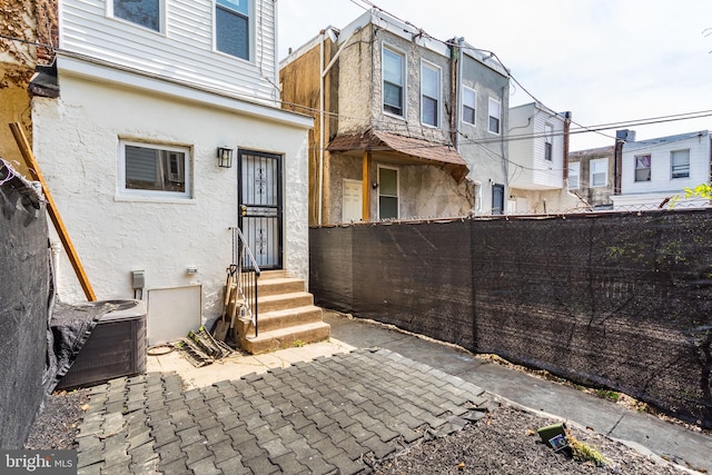 back of house featuring entry steps, a residential view, central air condition unit, stucco siding, and fence private yard