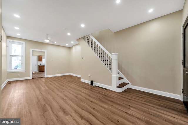 unfurnished living room featuring a ceiling fan, stairs, wood finished floors, and baseboards