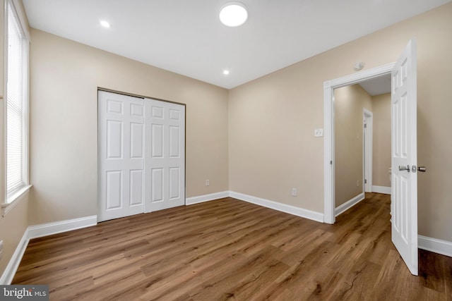 unfurnished bedroom featuring baseboards, recessed lighting, wood finished floors, and a closet