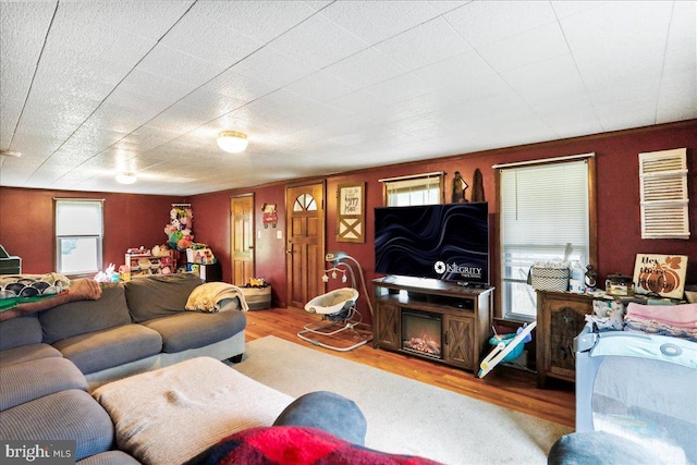 living area with plenty of natural light, a warm lit fireplace, and wood finished floors
