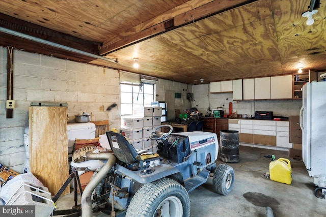 garage featuring freestanding refrigerator, concrete block wall, and wood ceiling