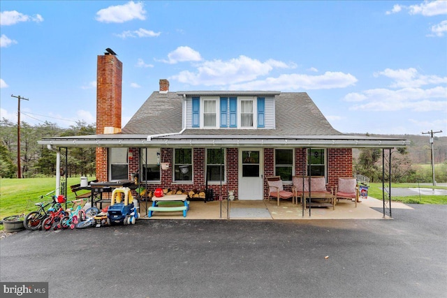 farmhouse-style home with roof with shingles, brick siding, and a chimney
