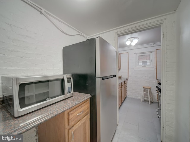 1234 Monroe St NE, Washington, DC 20017 - kitchen featuring brown cabinets, appliances with stainless steel finishes, light tile patterned flooring, and brick wall
