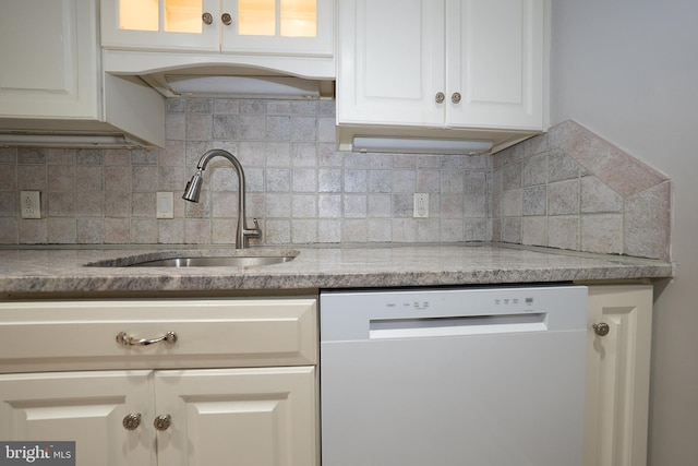 kitchen featuring white dishwasher, a sink, tasteful backsplash, white cabinetry, and glass insert cabinets