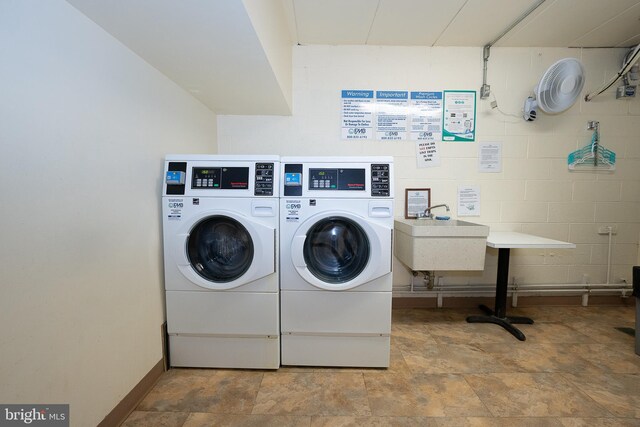 community laundry room featuring washing machine and clothes dryer, stone finish flooring, and concrete block wall