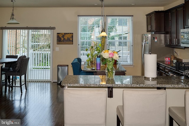 kitchen featuring dark wood-style flooring, appliances with stainless steel finishes, a kitchen bar, dark brown cabinetry, and dark stone counters