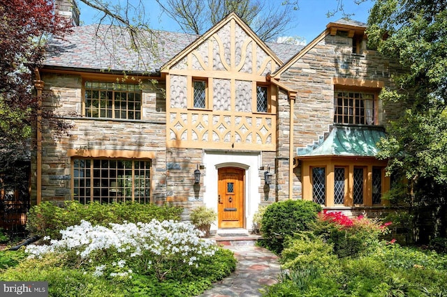 tudor-style house featuring a chimney and stone siding