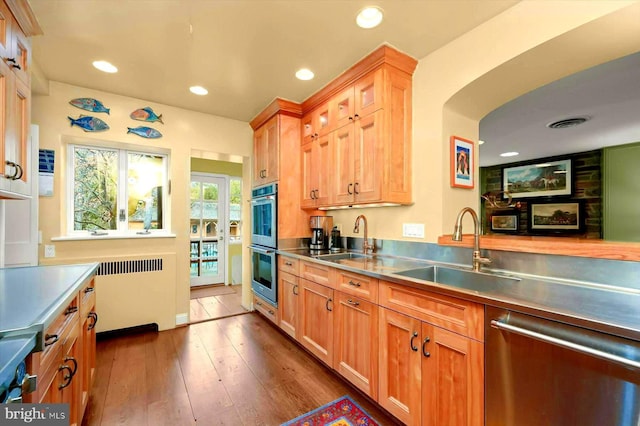kitchen with radiator heating unit, appliances with stainless steel finishes, a sink, and stainless steel countertops