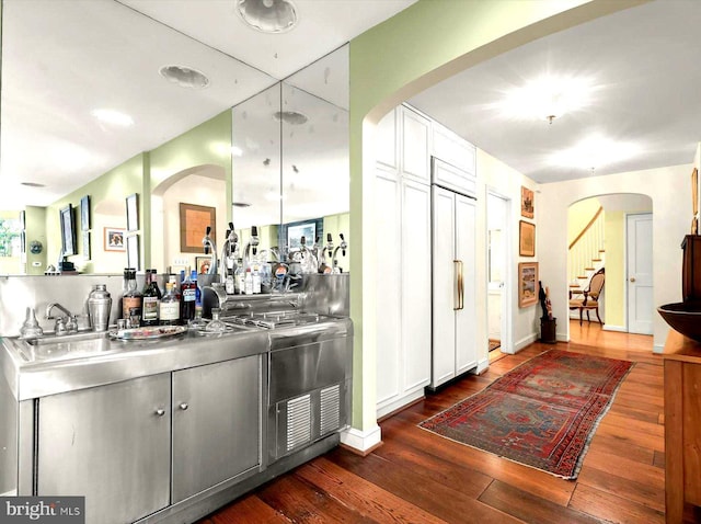 bar with paneled built in fridge, arched walkways, and dark wood-type flooring