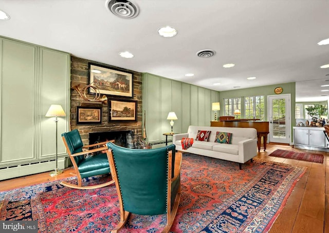 living room with baseboard heating, a stone fireplace, recessed lighting, visible vents, and hardwood / wood-style flooring