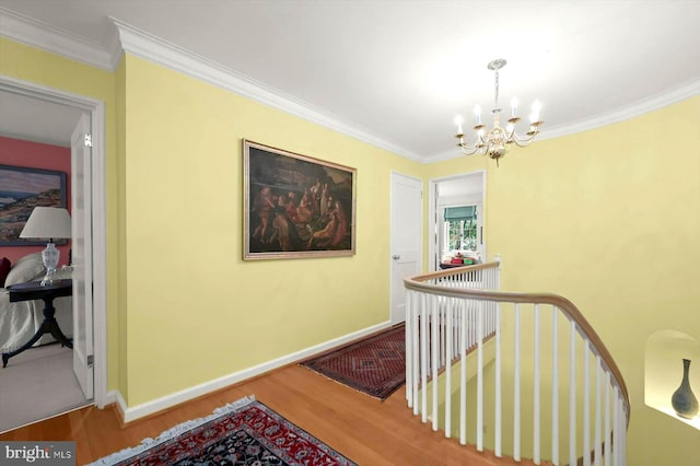 hall with an upstairs landing, wood finished floors, baseboards, a chandelier, and ornamental molding