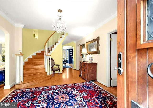 foyer entrance featuring crown molding, arched walkways, baseboards, and stairs