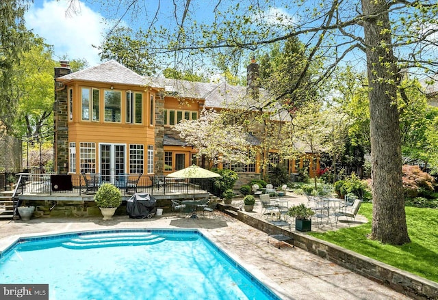 back of property featuring a fenced in pool, a patio area, a wooden deck, and a chimney