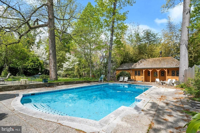 outdoor pool with an exterior structure, fence, an outbuilding, and a patio area
