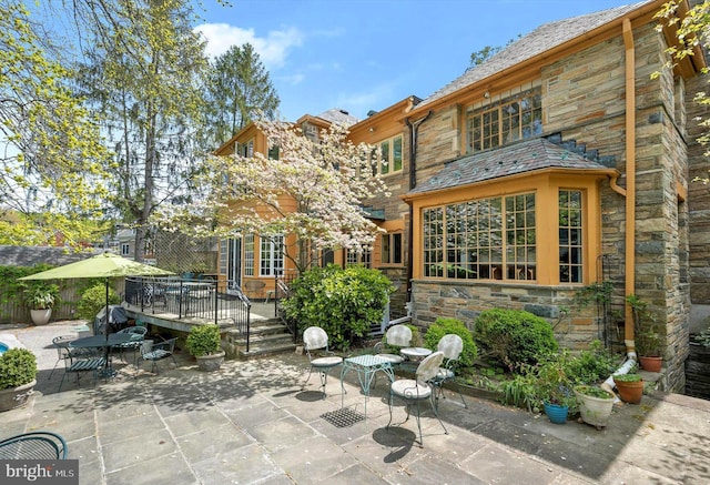 back of property with stone siding, a high end roof, a wooden deck, and a patio area