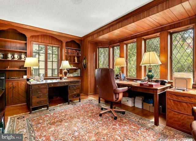 office with built in features, a textured ceiling, wood walls, and wood finished floors