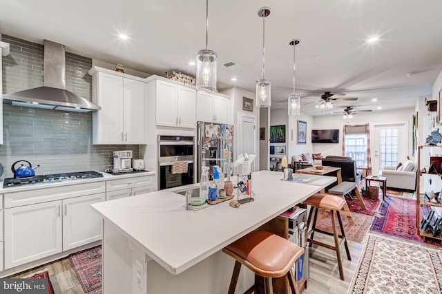 104 Saint Ives Pl Unit 409, Oxon Hill, MD 20745 - kitchen with a breakfast bar, light wood-style flooring, wall chimney exhaust hood, decorative backsplash, and appliances with stainless steel finishes