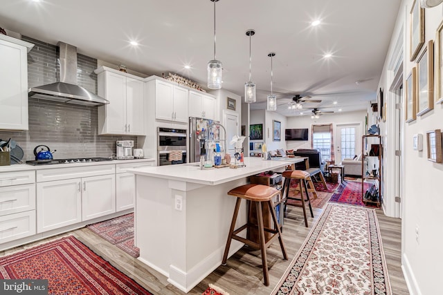 104 Saint Ives Pl Unit 409, Oxon Hill, MD 20745 - kitchen with wall chimney range hood, open floor plan, appliances with stainless steel finishes, light wood-style floors, and backsplash