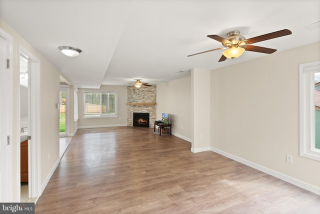 unfurnished living room featuring a stone fireplace, light wood-style floors, ceiling fan, baseboards, and visible vents