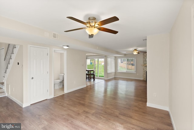 unfurnished living room featuring stairway, wood finished floors, ceiling fan, baseboards, and visible vents