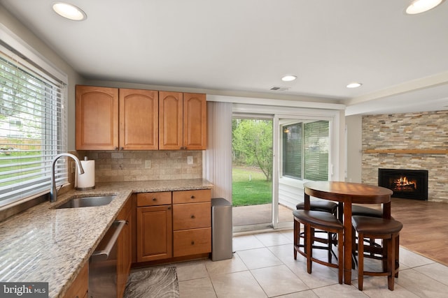 kitchen with stainless steel dishwasher, light stone counters, a stone fireplace, a sink, and visible vents