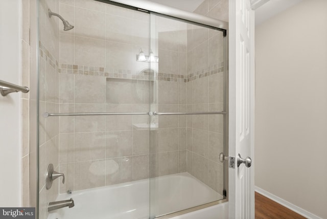 full bath with wood finished floors, baseboards, and shower / bath combination with glass door
