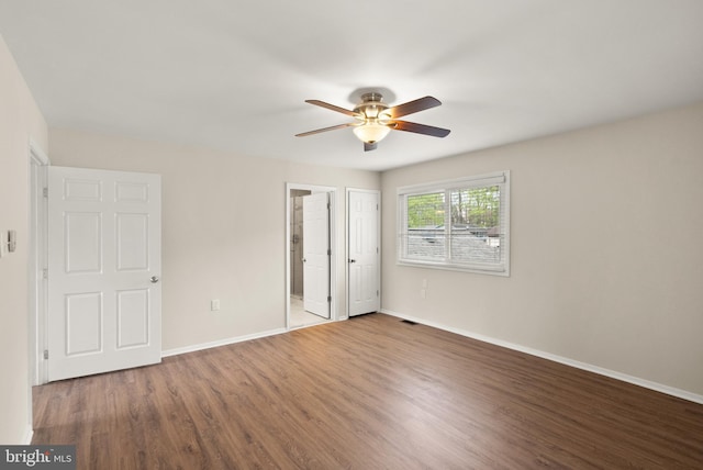 unfurnished bedroom featuring ceiling fan, baseboards, wood finished floors, and ensuite bathroom