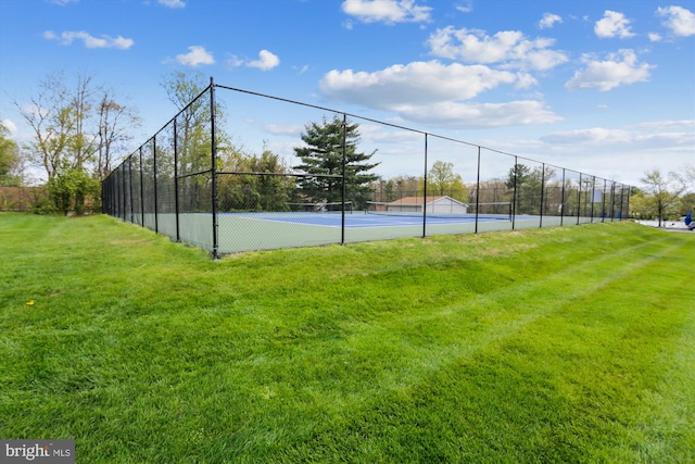 view of tennis court with fence and a yard