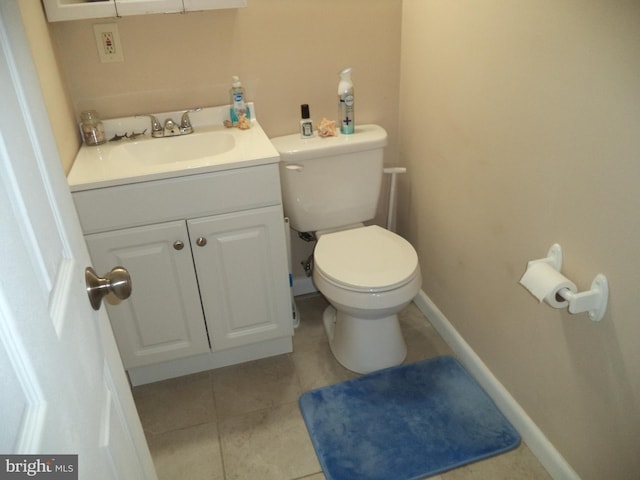 half bathroom featuring toilet, tile patterned floors, vanity, and baseboards