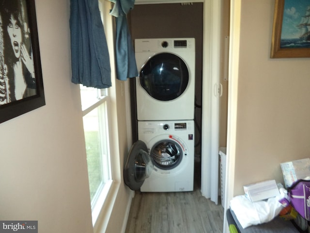 clothes washing area featuring stacked washer / dryer, laundry area, and wood finished floors