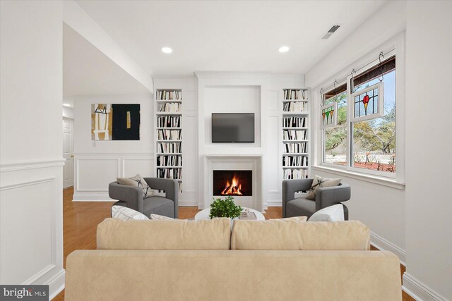 1506 N Bay Shore Dr, Milton, DE 19968 - living room featuring a lit fireplace, built in features, visible vents, a decorative wall, and wood finished floors