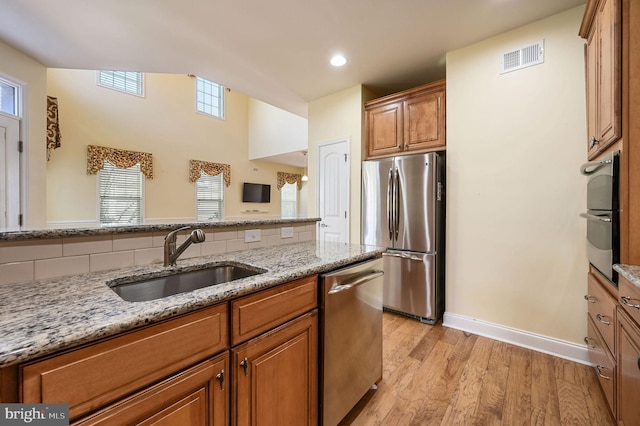 105 Arch St, Milton, DE 19968 - kitchen featuring light stone countertops, brown cabinetry, light wood-style flooring, appliances with stainless steel finishes, and a sink