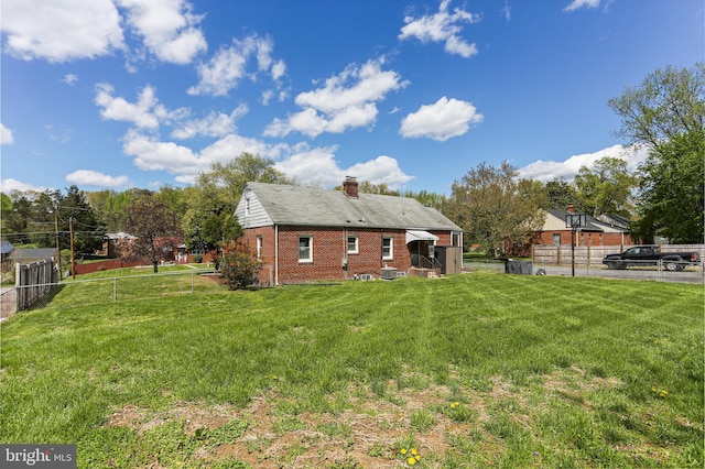 rear view of property featuring fence, a chimney, brick siding, and a yard