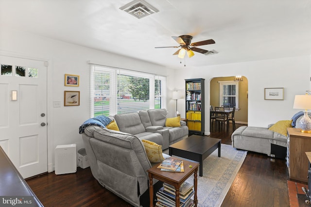 living area featuring visible vents, arched walkways, ceiling fan, and dark wood finished floors