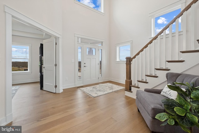 entrance foyer with stairway, a high ceiling, baseboards, and light wood-type flooring