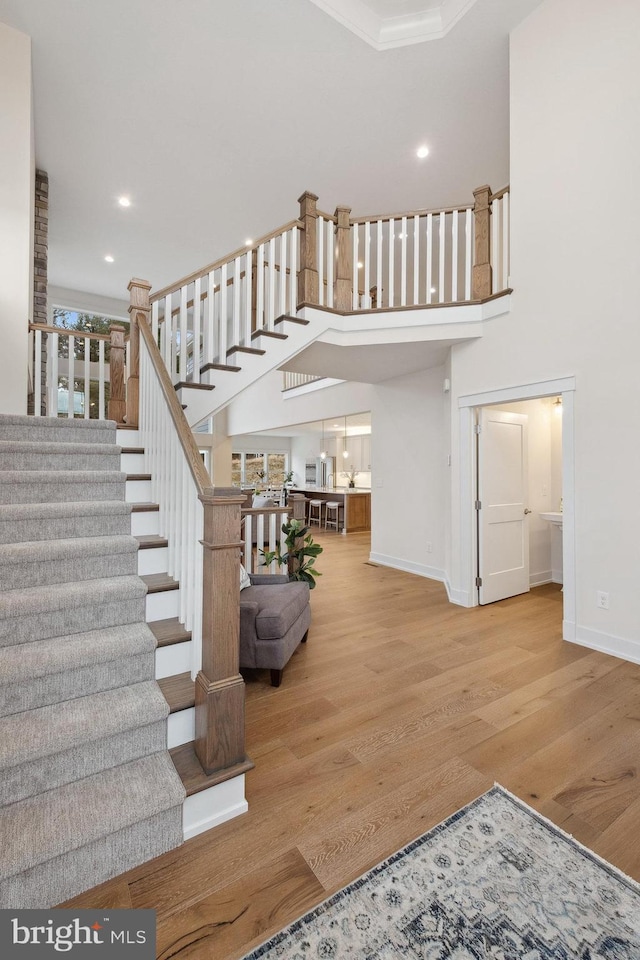 stairs with wood finished floors, crown molding, baseboards, a towering ceiling, and recessed lighting