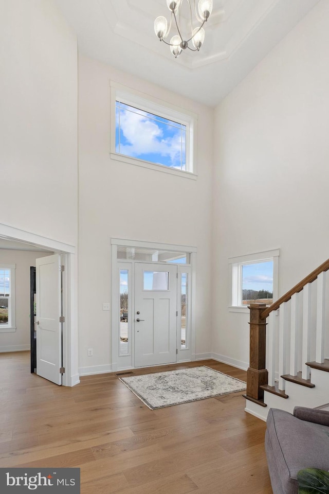 foyer entrance with stairway, a chandelier, light wood-type flooring, and a towering ceiling