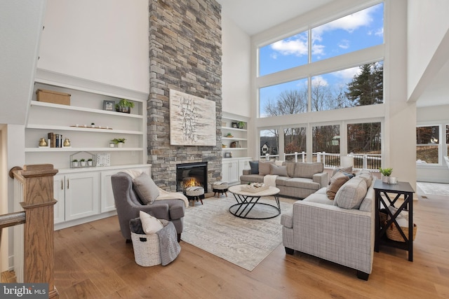 living area with a fireplace, a towering ceiling, light wood-type flooring, and built in shelves