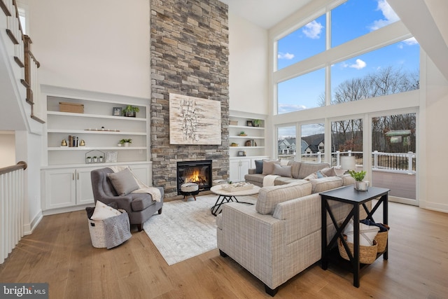 living area with a fireplace, a towering ceiling, plenty of natural light, and wood finished floors