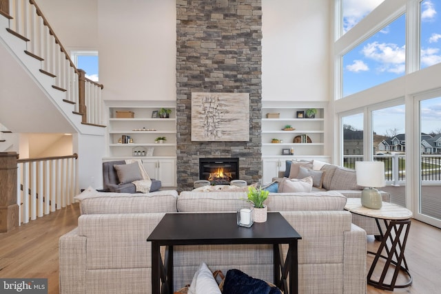 living room featuring a fireplace, a towering ceiling, a healthy amount of sunlight, and wood finished floors