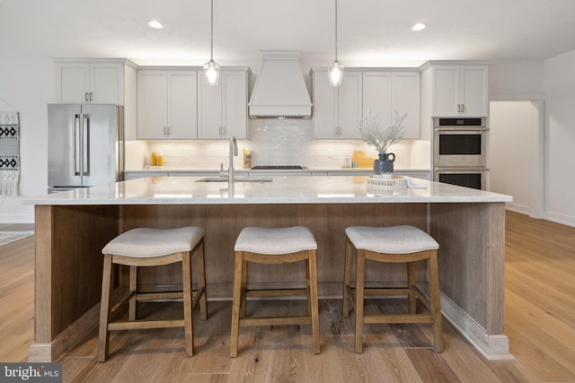 kitchen featuring light wood-style flooring, a sink, appliances with stainless steel finishes, tasteful backsplash, and custom exhaust hood