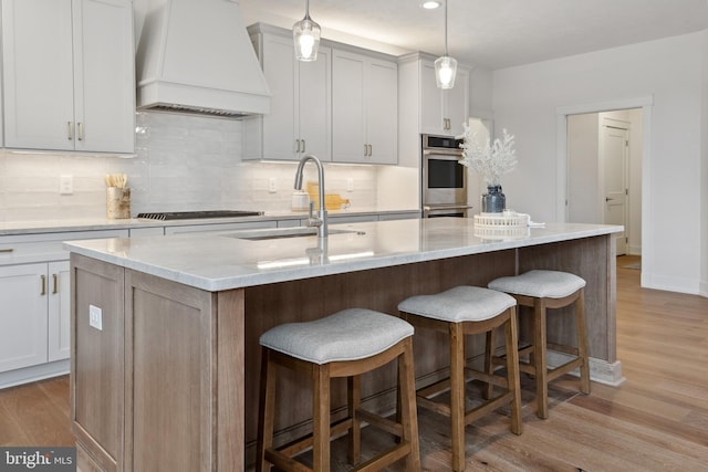 kitchen with gas stovetop, backsplash, light wood-type flooring, and custom range hood