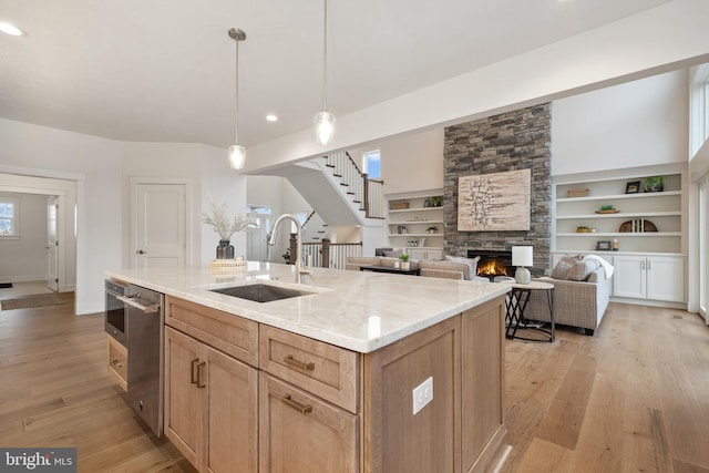 kitchen with a sink, light stone counters, a fireplace, stainless steel dishwasher, and light wood-style floors