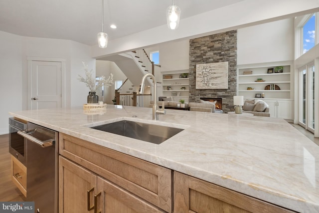kitchen with a sink, a fireplace, pendant lighting, open floor plan, and light stone countertops